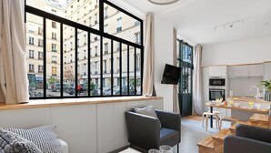 Eine moderne Wohnung mit großem Fenster, Flachbildfernseher, Essbereich und einer Küchenzeile.