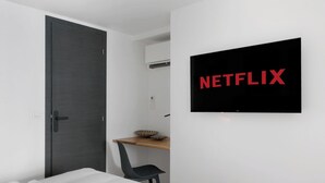 Ein modernes Zimmer mit einer dunklen Tür, einem kleinen Holztisch mit einem Stuhl und einem an der Wand befestigten Fernseher, der 'NETFLIX' anzeigt.