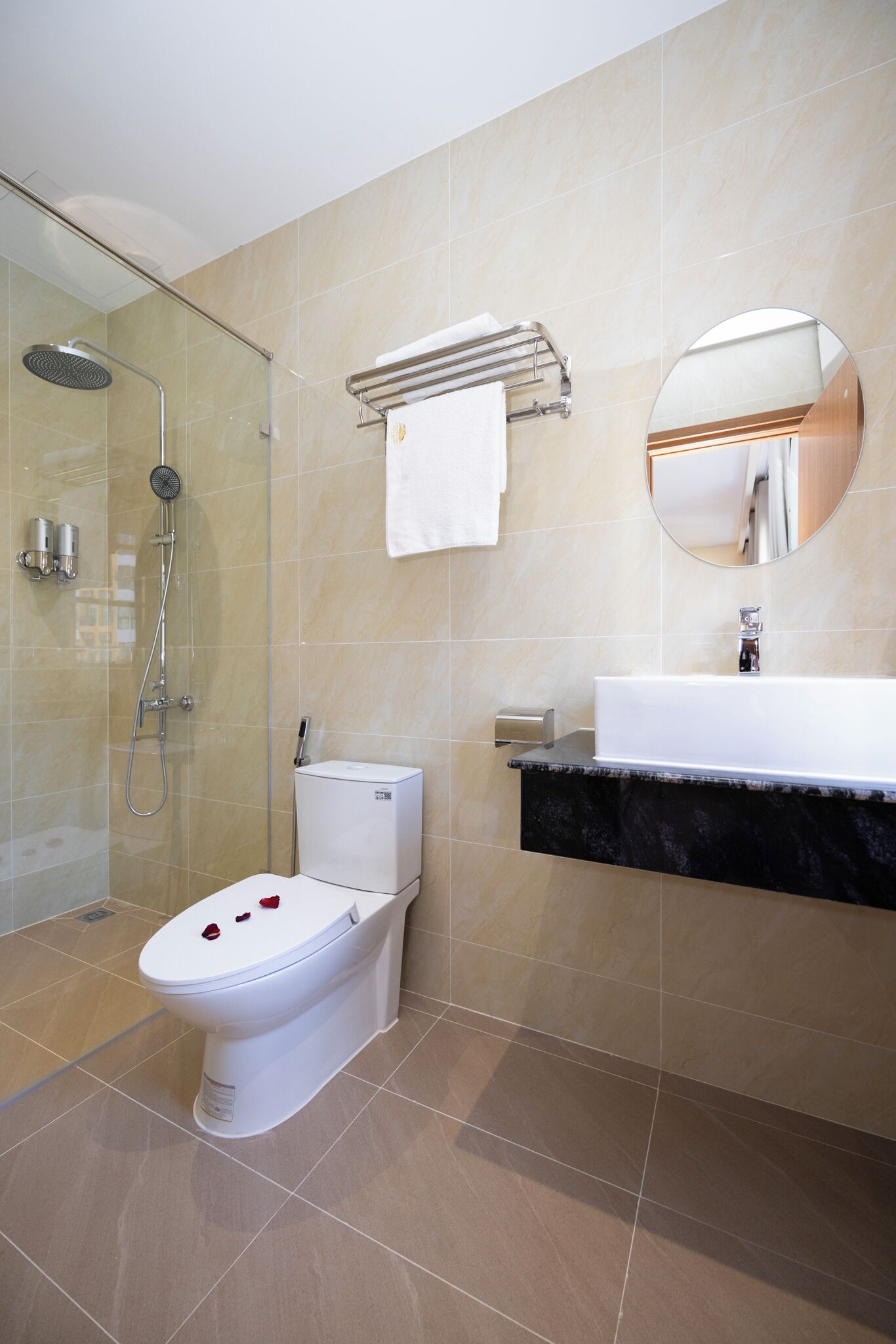 A modern bathroom with a glass-enclosed shower, a white toilet, a sink with a marble countertop, and a round mirror.