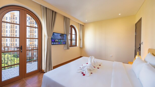 A hotel room with a bed, a TV, a window with curtains, and a view of buildings outside. - Golden Sand Phu Quoc Hotel (Phu Quoc)