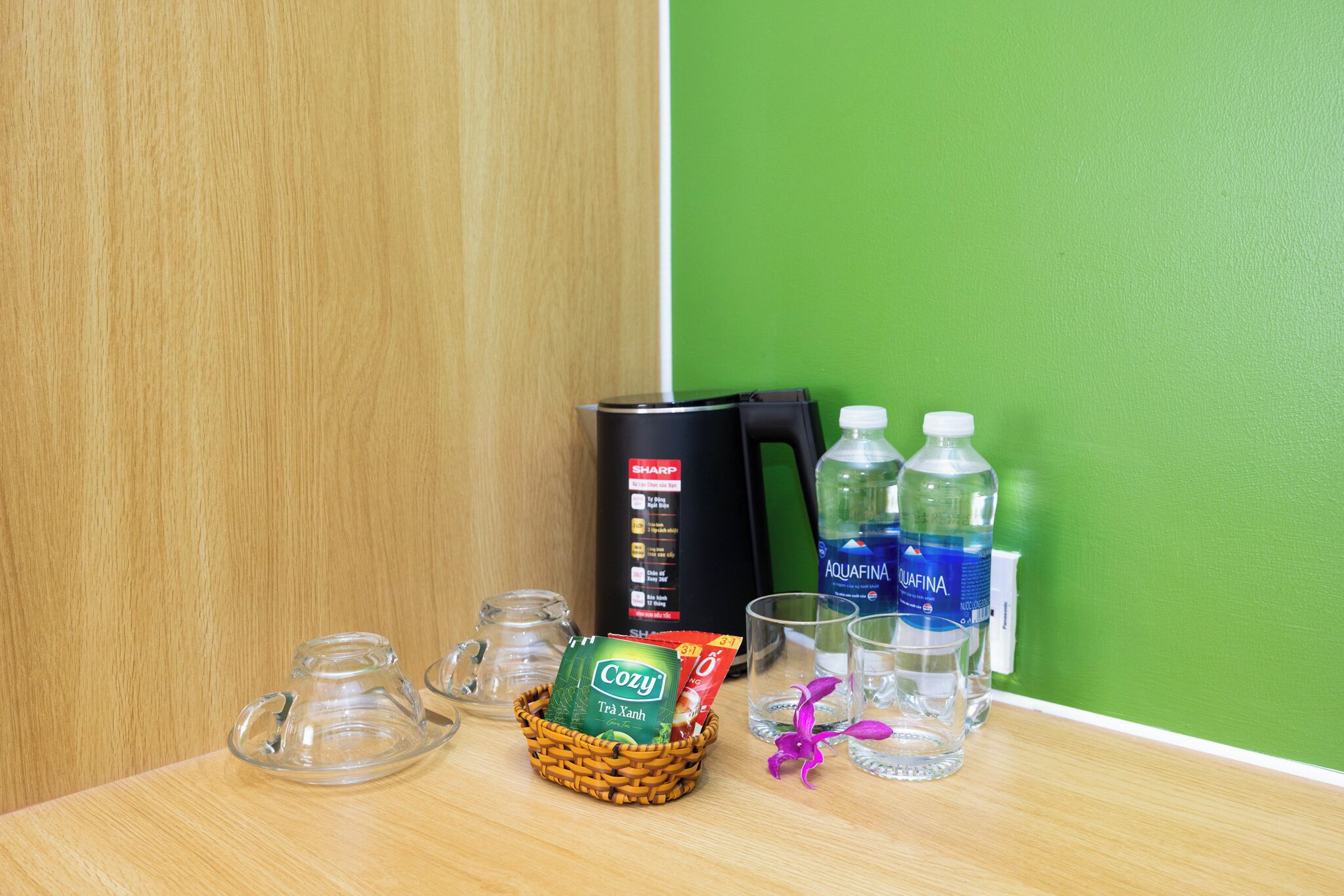 A wooden table with a basket of items, including a coffee maker, water bottles, and glasses.