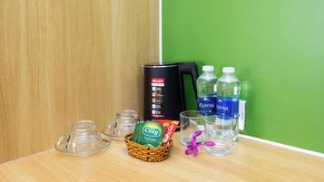 A wooden table with a basket of items, including a coffee maker, water bottles, and glasses.