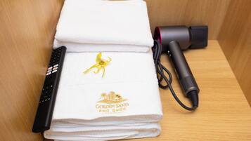 A folded white towel with a logo, a remote control, and a hairdryer on a wooden surface.