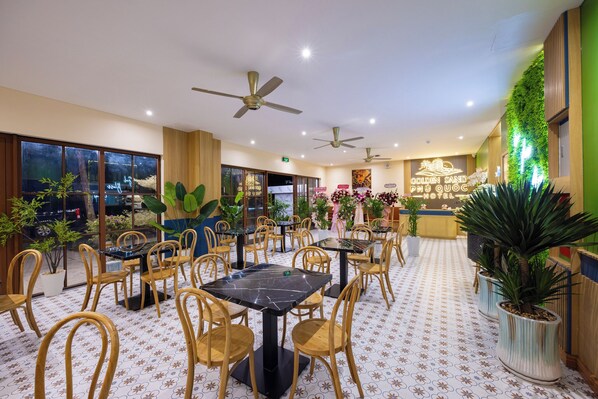 Un vestíbulo de hotel con varias mesas de comedor, sillas, ventiladores de techo y plantas en macetas.