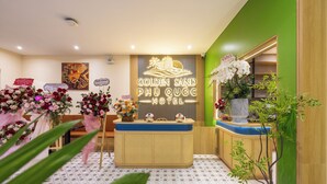 A hotel reception area with a reception desk, floral arrangements, and a neon sign for the hotel. - Golden Sand Phu Quoc Hotel (Phu Quoc)