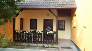 A building with a yellow facade, a wooden balcony with flower pots, and a tiled roof. - Kisház klímával, Wifivel max. 4 fős családoknak, 8 percre a Balatontól! (Balatonboglár)