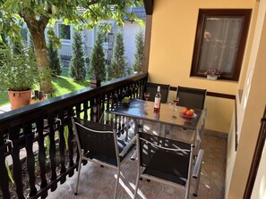 Un balcon avec une table en verre, deux chaises, une bouteille de vin et une assiette de fruits.