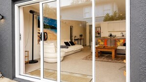 A modern home interior with a sliding glass door leading to a living room, a sofa, a coffee table, and a kitchen area visible through the glass.