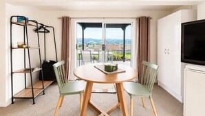 A room with a round table, two chairs, a TV, a wardrobe, a shelf unit, and a view through a window.