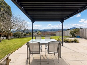 A covered patio with a table and chairs, a view of a backyard, and a wooden fence.