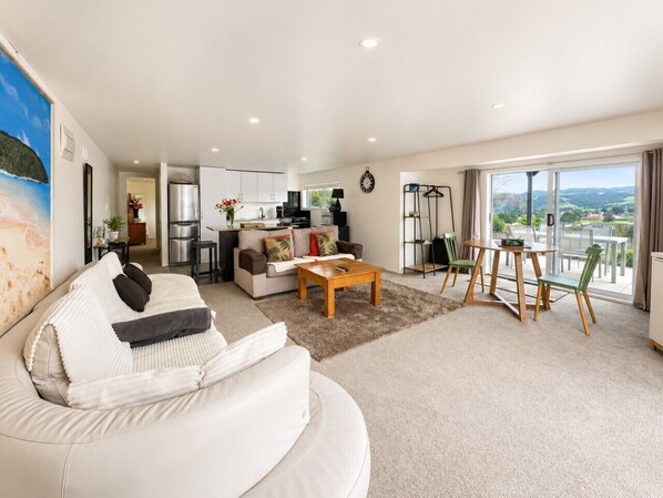 A spacious living room with a sofa, coffee table, and a balcony with a view. - Stylish 1BR Retreat | Patio | Walk to Shops | Parking (Whangārei)