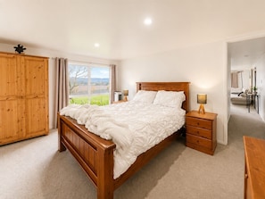 A bedroom with a wooden bed, bedside tables, a wardrobe, and a window with curtains.