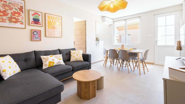 Ein modernes Wohnzimmer mit grauem Sofa, rundem Holztisch und einem Essbereich mit weißem Tisch und Stühlen.