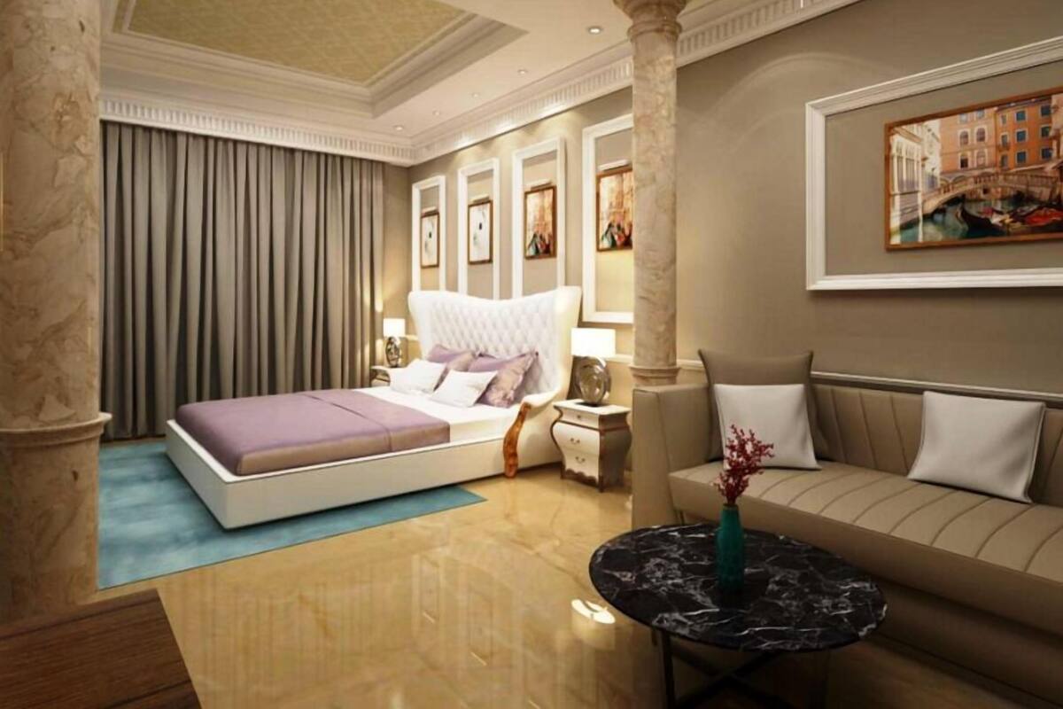 A hotel room with a bed, a sofa, a round table, and a painting on the wall.