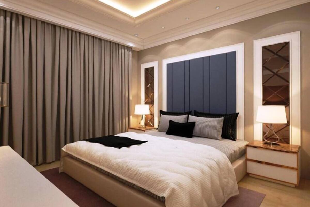 A modern hotel room with a large bed, bedside tables, and a headboard with built-in lighting.