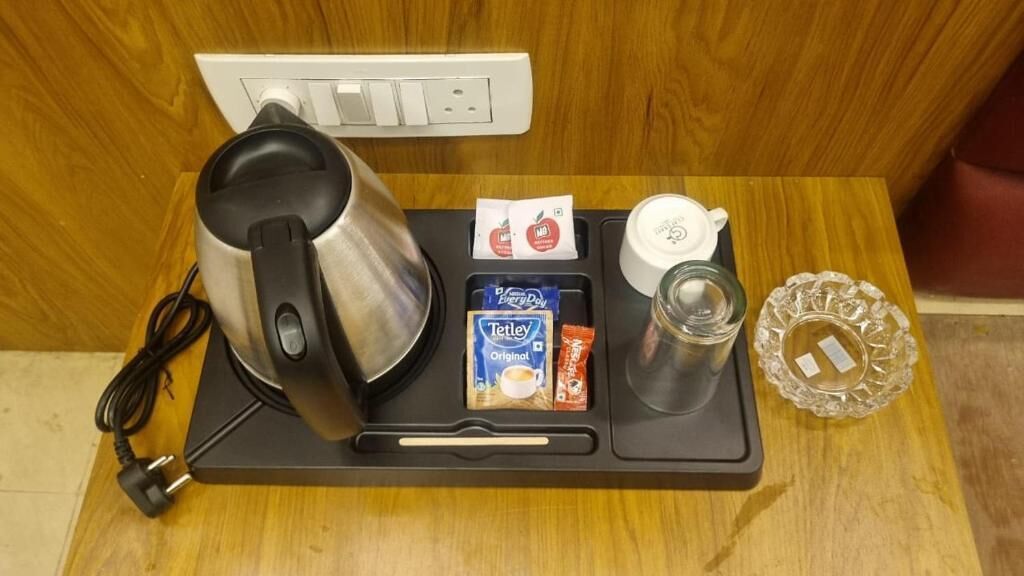 Une machine à café, une bouilloire, une tasse, un plateau avec des dosettes de café et un verre, le tout posé sur une surface en bois.