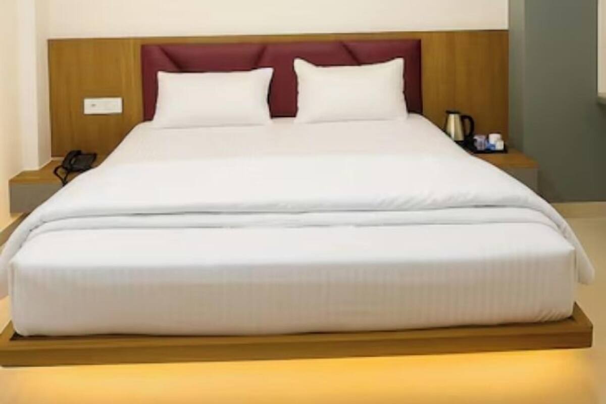 A modern hotel room with a large bed, wooden headboard, bedside tables, and a ceiling light fixture.