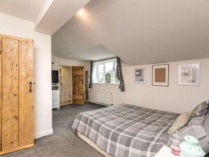 Ein Schlafzimmer mit einem Bett, einem Holzschrank, einem Fenster mit Vorhängen und gerahmten Bildern an der Wand.