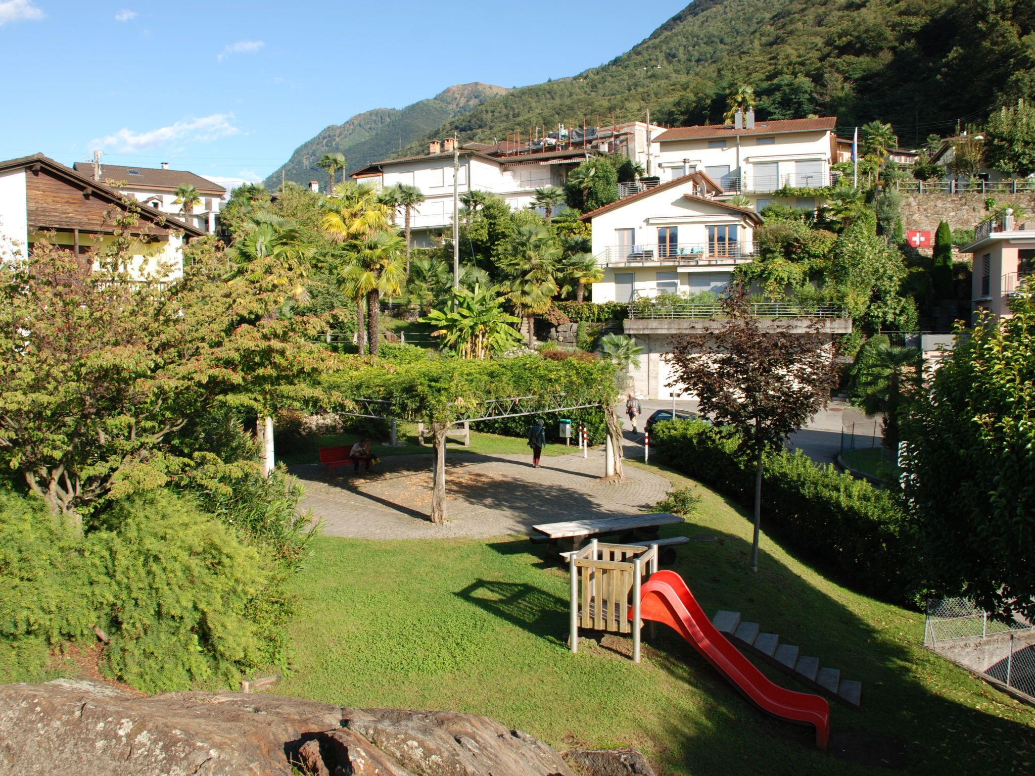Bairro residencial com casas, um parquinho com escorrega e uma montanha ao fundo.