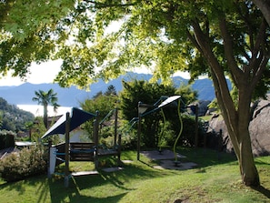Ein Spielplatz mit Klettergerüsten und einer Bank, umgeben von Bäumen und mit Blick auf Berge.