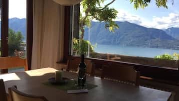 Uma mesa de jantar com cadeiras, uma vela e uma garrafa, em frente a uma janela com vista para montanhas e um lago.