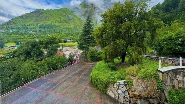A mountainous landscape with a paved pathway, greenery, and a stone wall.
