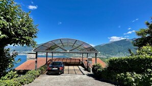 A covered parking area with a car, surrounded by greenery and a mountainous backdrop. - Casa Poggio Verde by Interhome (Magadino)