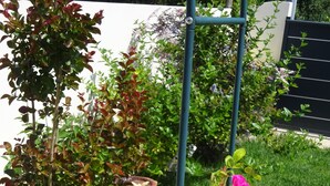 A garden with a trellis supporting pink flowers, a small tree, and a birdbath. - Cosy & quiet studio with private parking, near ocean and town center. (La Rochelle 17000)