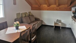 Ein gemütliches Zimmer mit Holzboden, einer Couch mit Kissen, einem Esstisch mit Stühlen und einem kleinen Beistelltisch.