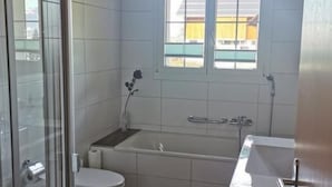 Ein Badezimmer mit Duschkabine, Toilette, Badewanne und einem Fenster über der Badewanne.