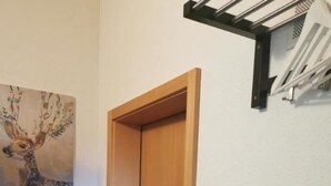 Ein Flur mit einer Holztür, einer weißen Vase mit rosa Blumen und einem Bild von einem Reh an der Wand.