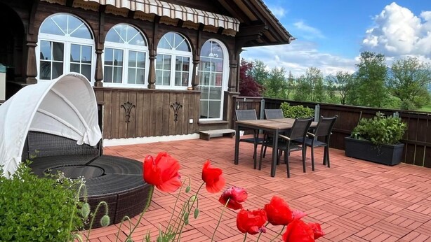 Une terrasse en bois dotée d’un espace salon couvert, d’une table et de chaises.