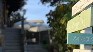 Un panneau indicateur en bois, doté de flèches indiquant les directions vers « Pargolies », « Zauber », « plage » et « Wohlfühlhaus ».
