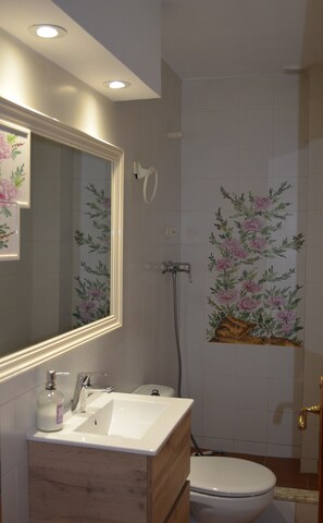 Une salle de bain équipée d’un lavabo, d’un miroir, de toilettes, d’une douche et de carreaux muraux à motifs floraux.