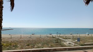 Uma praia com vista clara do mar, um calçadão de madeira e uma placa.