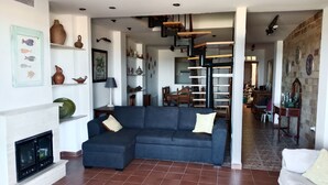 Uma sala de estar com sofá em formato de L, lareira e área de jantar ao fundo.