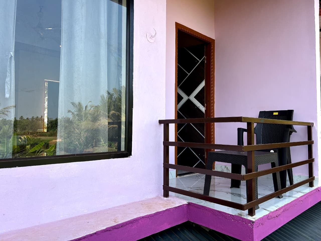 A balcony with a wooden railing, a door, and two chairs.