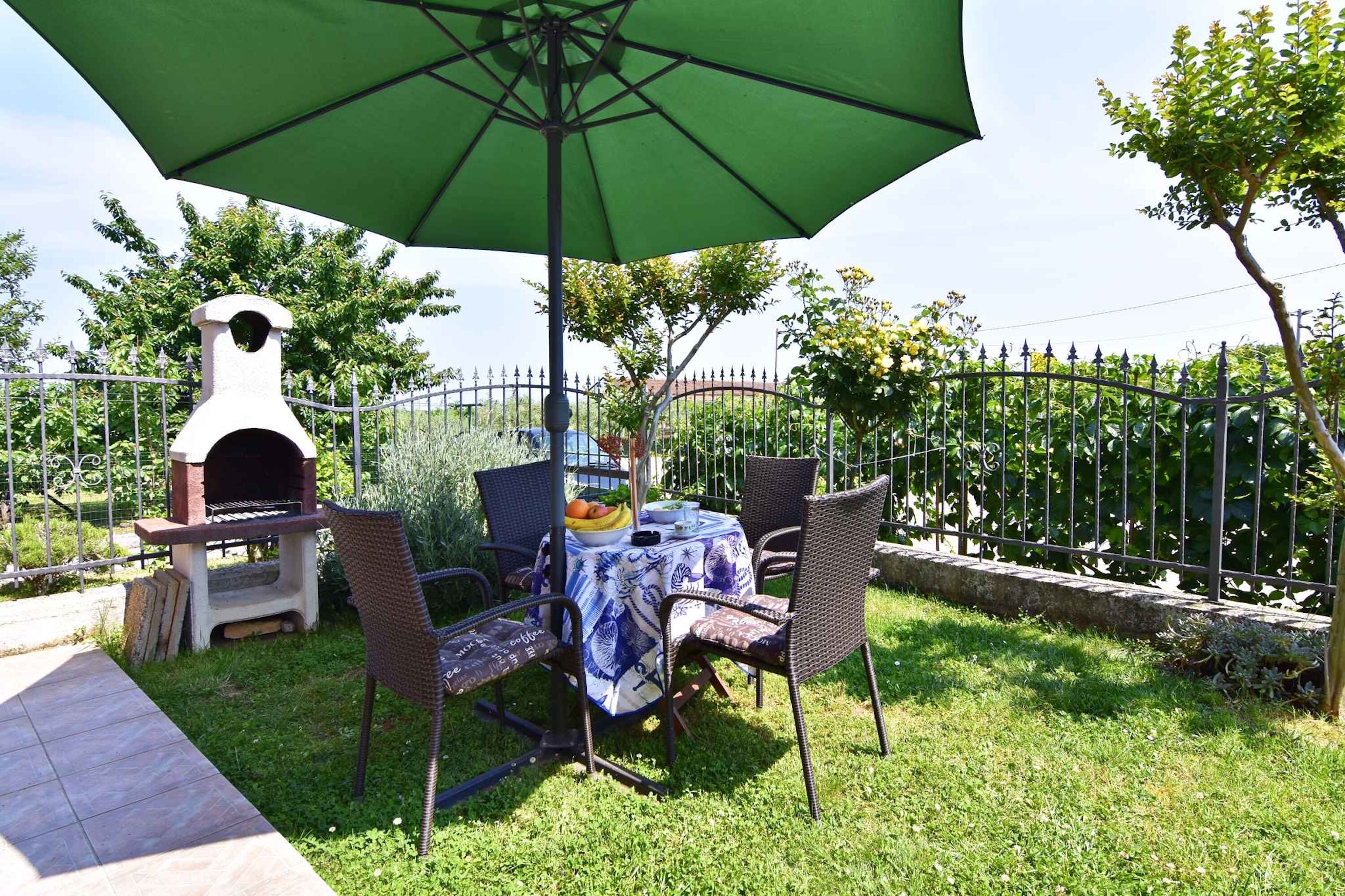 An outdoor patio with a table, chairs, a grill, and a green umbrella.
