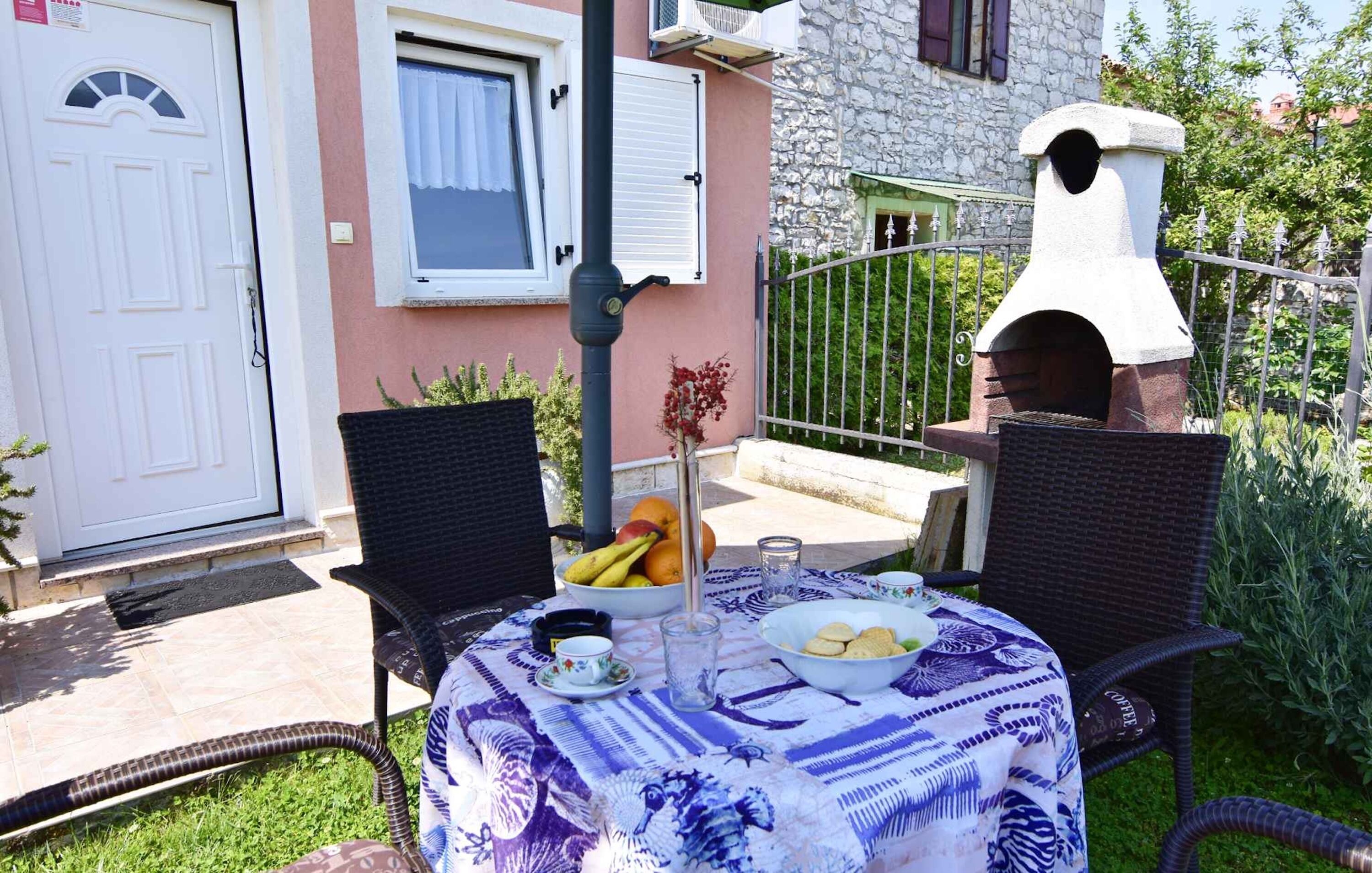 A patio with outdoor seating, a table set with food and drinks, a stone building, and a brick oven.