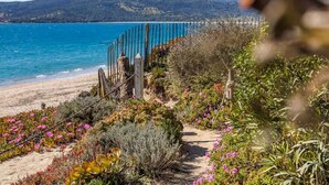 A coastal garden with a pathway leading to a beach, surrounded by diverse vegetation and a clear view of the sea and distant hills. - Luxury Beachfront Studio - Panoramic sea view - Direct beach access - Corsica (Olmeto)
