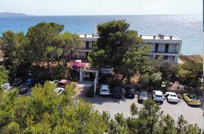 Um edifício costeiro com área de estacionamento, árvores e vista para o mar.