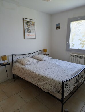 A bedroom with a bed, two bedside lamps, a radiator, a window with a leaf pattern, and a poster on the wall. - Gîte avec piscine privée situé à Uzès (Uzès)