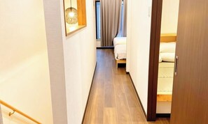 A narrow hallway with wooden flooring, a bed with white bedding, and a hanging light fixture.