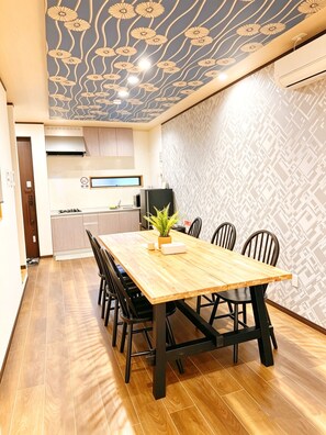 Un coin repas avec une table en bois, des chaises noires, une plante en pot et une cuisine en arrière-plan.