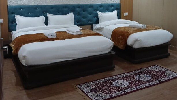 A hotel room with two beds, a blue headboard, a patterned rug, and a hanging light fixture. - Hotel Shree Jee Inn (Badrinath)