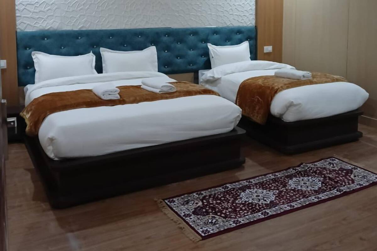 A hotel room with two beds, a blue headboard, a patterned rug, and a hanging light fixture.