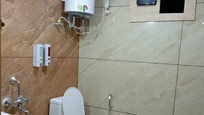 A bathroom with a toilet, a sink, a shower, and a water heater. - Hotel Shree Jee Inn (Badrinath)