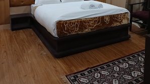 A bedroom with a large bed, a headboard, a wooden floor, a patterned rug, and a ceiling light. - Hotel Shree Jee Inn (Badrinath)