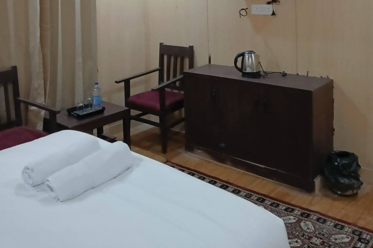 A hotel room with a bed, a desk with a kettle, a chair, a TV mounted on the wall, and a curtain.
