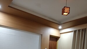 A neatly made bed with white linens and a brown headboard, a wooden floor, a patterned rug, and a hanging light fixture. - Hotel Shree Jee Inn (Badrinath)